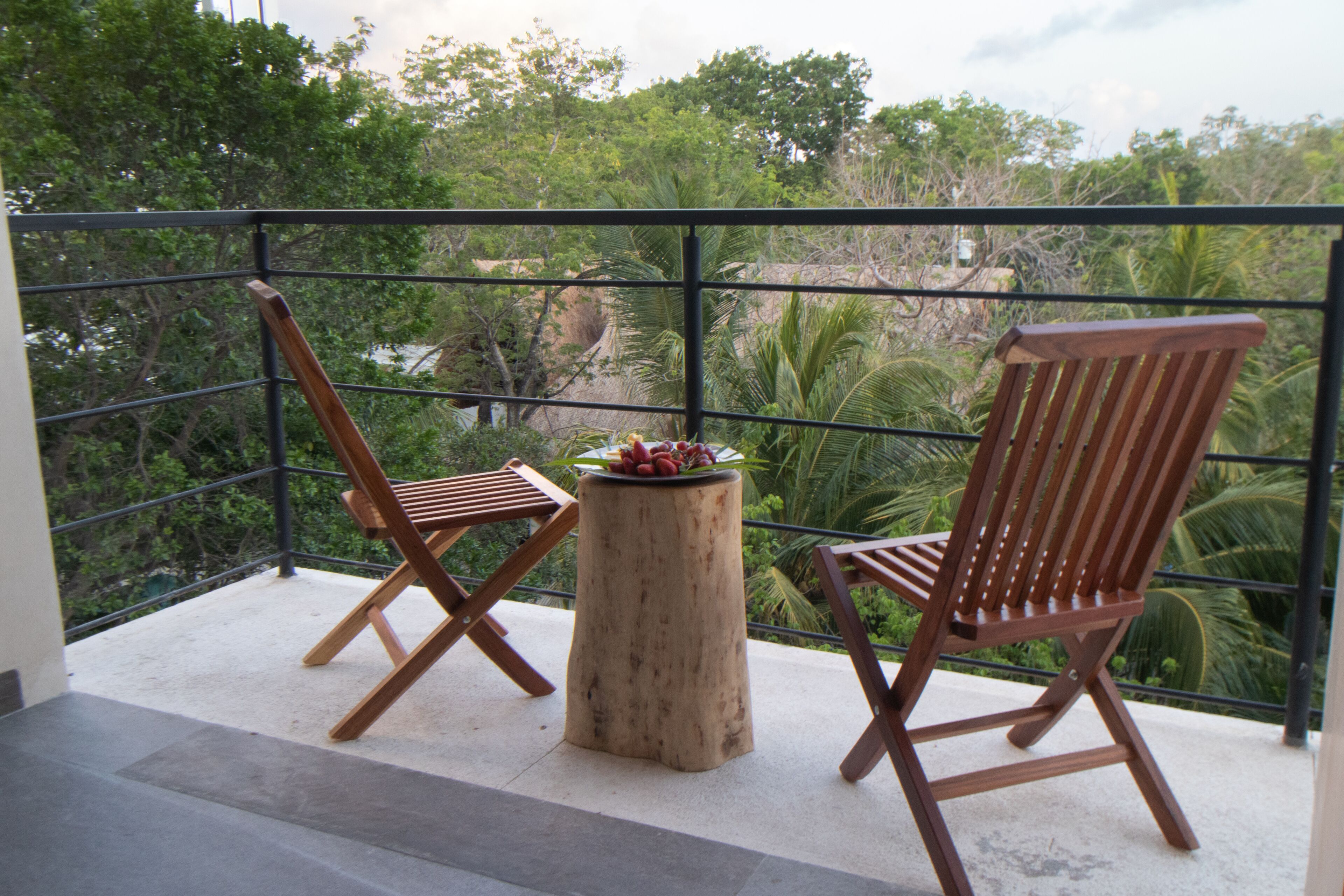 A balcony with two wooden chairs and a small round table with fruit.