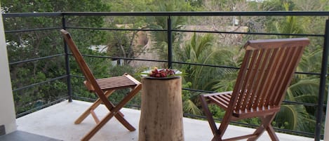 A balcony with two wooden chairs and a small round table with fruit.