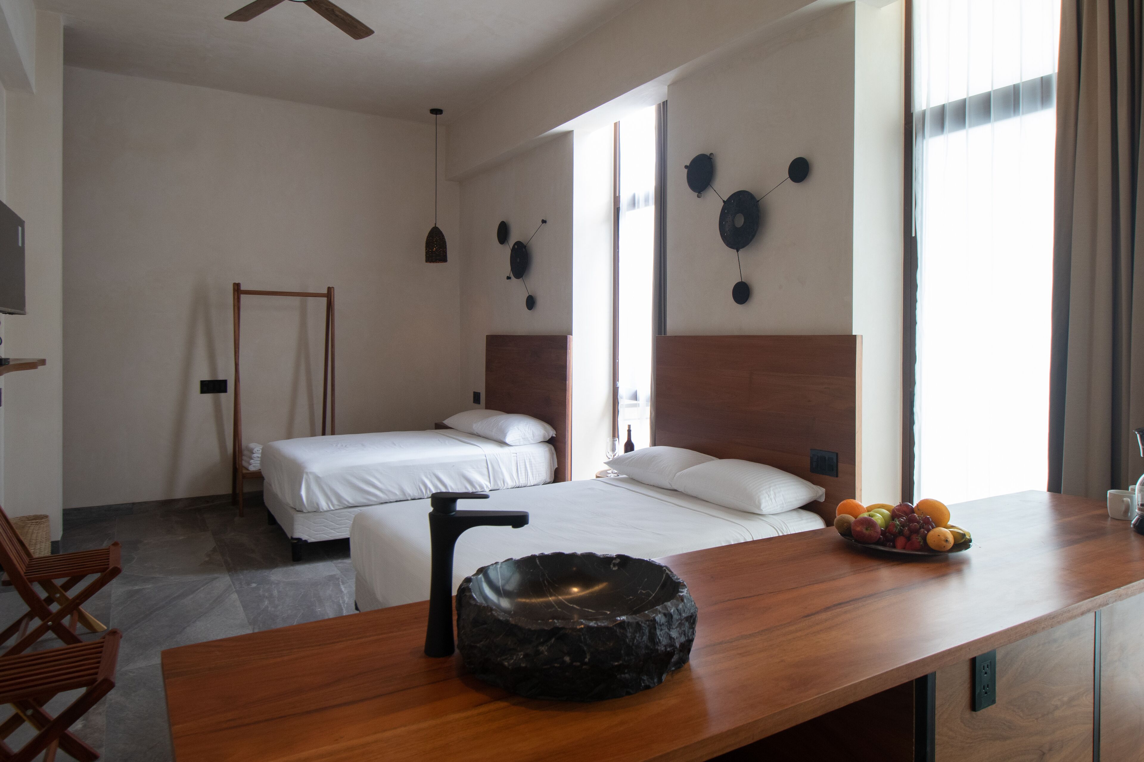 A hotel room with two beds, a wooden desk with a bowl sink, and a fruit bowl on the desk.