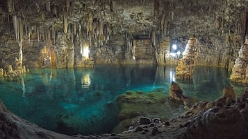 Una cueva con estalactitas y estalagmitas, agua cristalina y suelo rocoso.