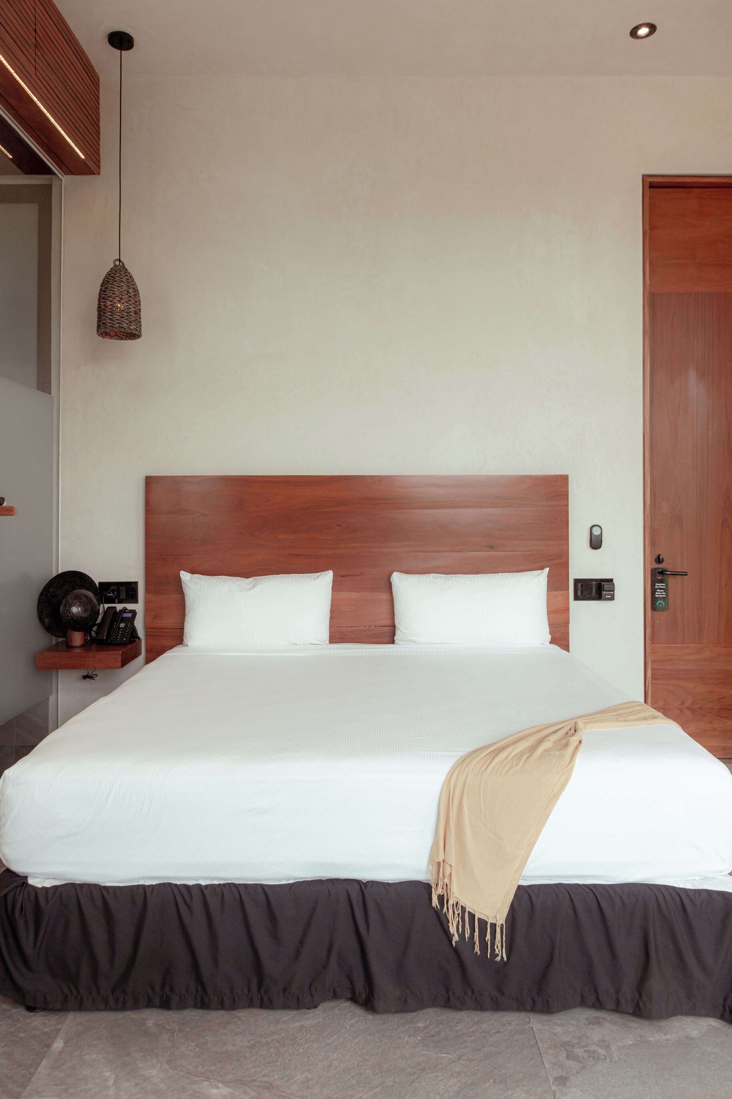 A modern hotel room with a large bed, wooden headboard, and a bedside table with a lamp.