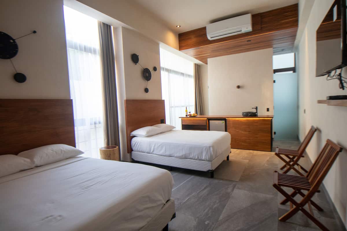 A hotel room with two beds, a wooden headboard, a desk with a chair, a mirror, and a window with curtains.