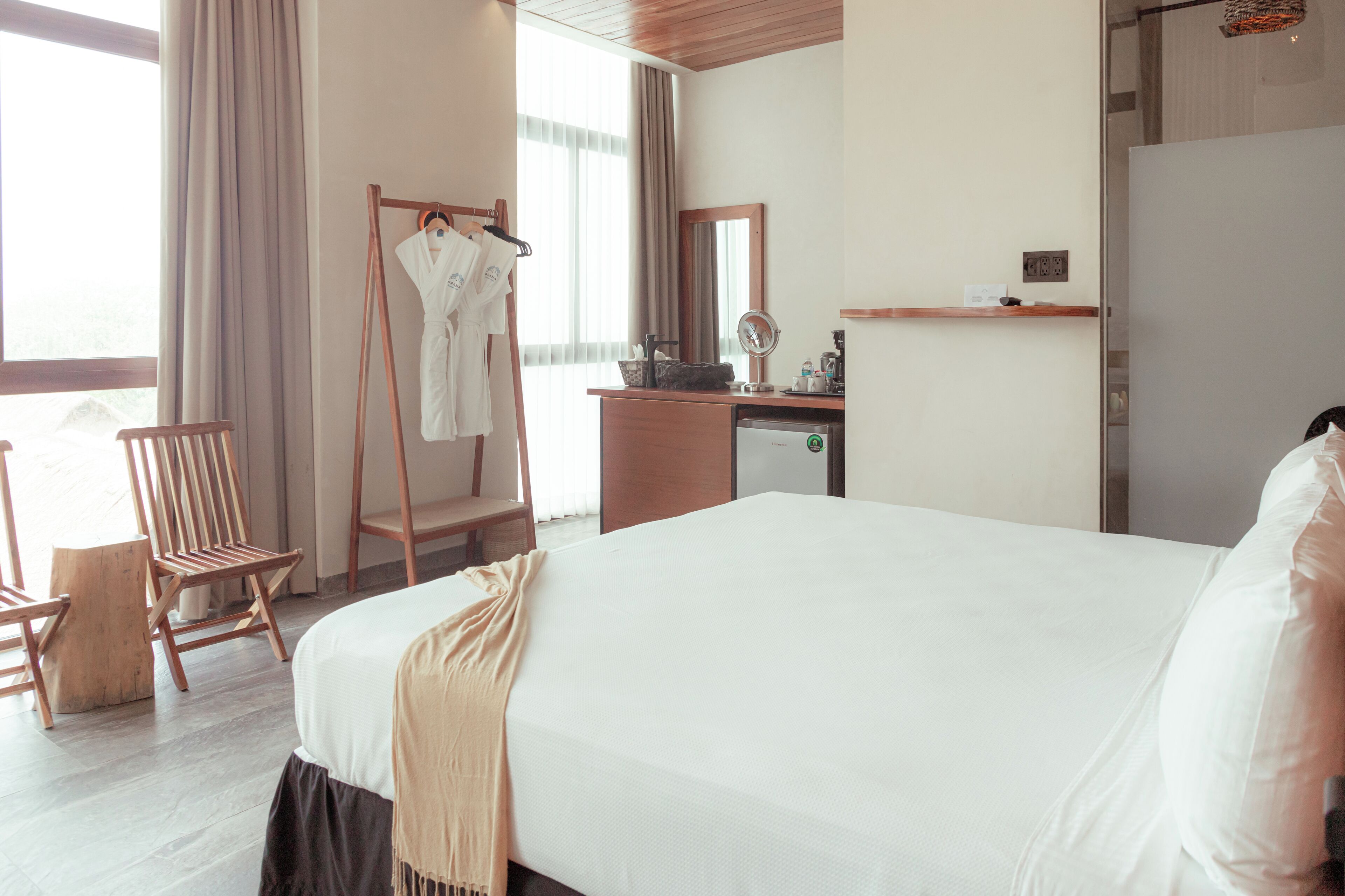 A hotel room with a large bed, a wooden chair, a desk with a mirror, and a wardrobe.