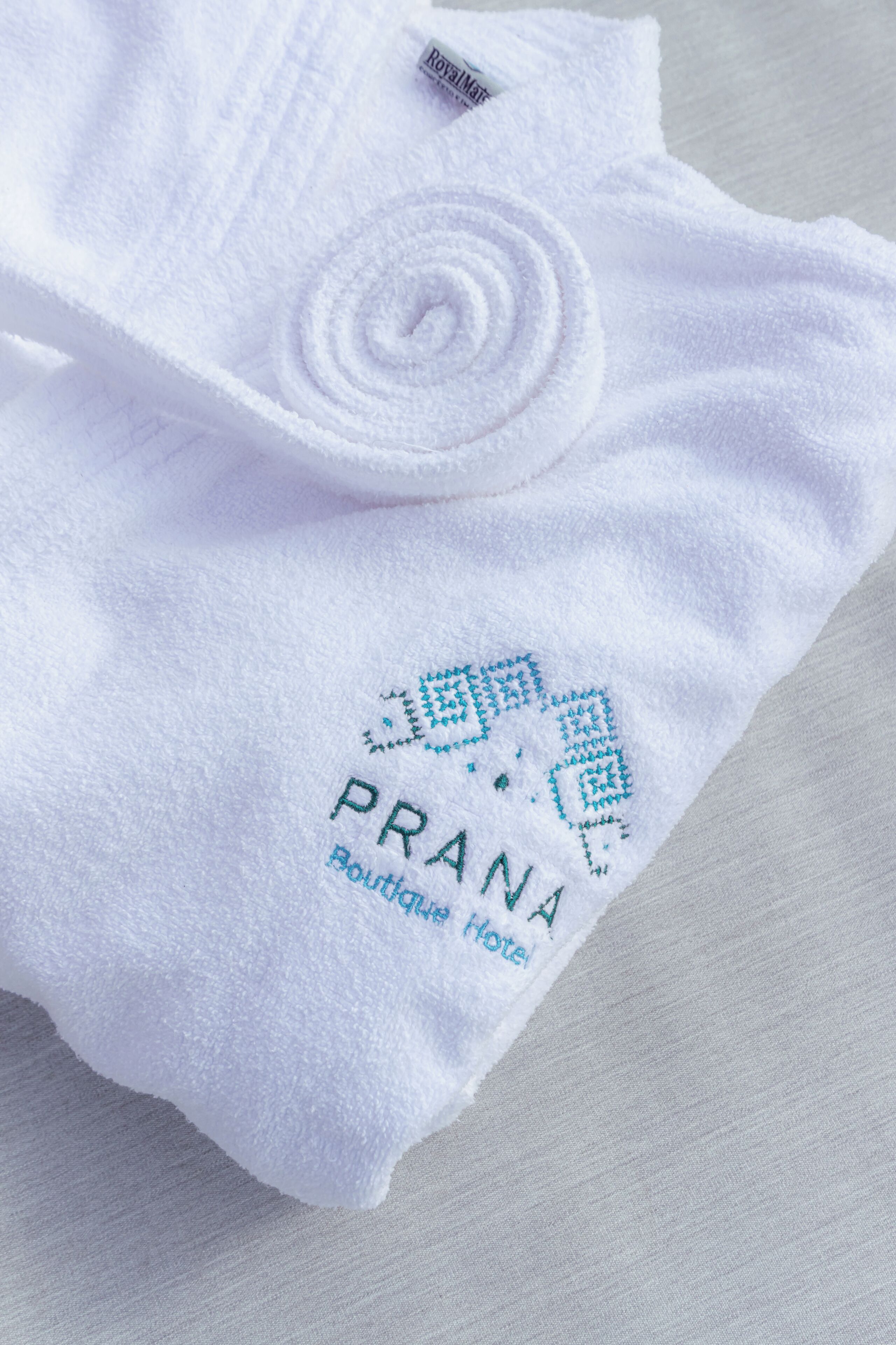 A white towel with a logo and text reading "PRANA Boutique Hotel".
