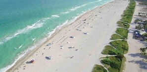 An aerial view of a beach with rows of umbrellas and sun loungers, a sandy shore, and a clear blue sea.