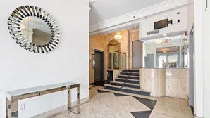 A modern lobby with a round mirror, a wooden bench, a staircase, and a reception desk.