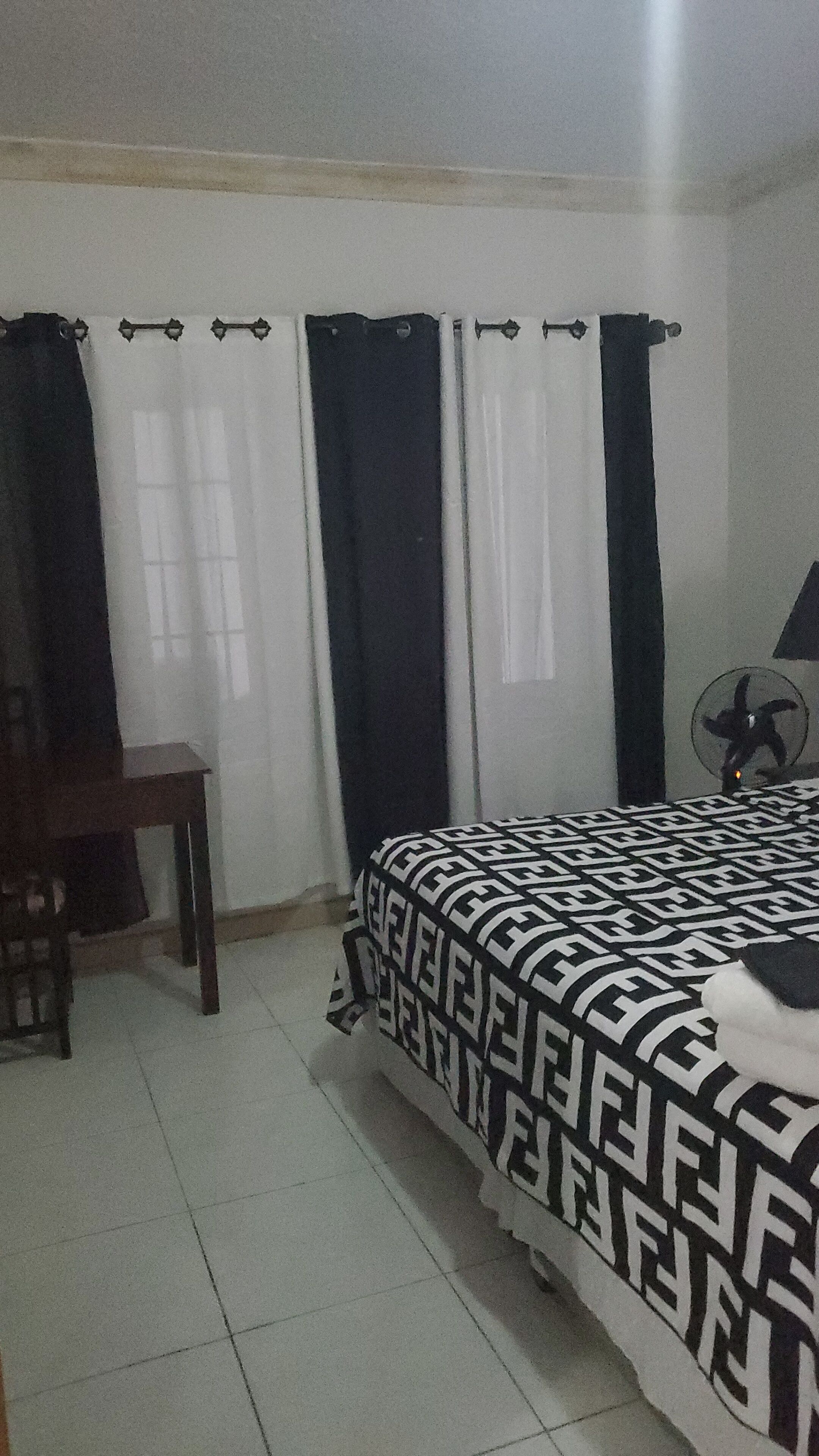 A bedroom with a bed, a chair, a fan, and curtains.