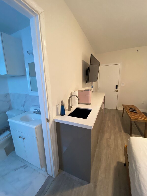 A compact kitchen with a sink, countertop, and a television mounted above it.