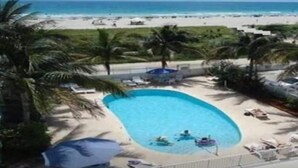 Piscina con vista a la playa y al océano, rodeada de palmeras y sillas de descanso.