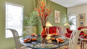 A dining area with a glass table, red upholstered chairs, and a vase with decorative branches. - Exquisite Townhome in Emerald Island: A Perfect Blend of Luxury and Comfort (Kissimmee)