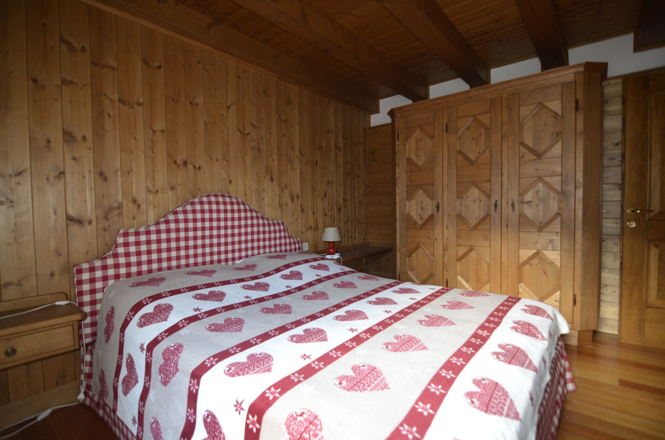 A wooden-paneled bedroom with a bed, nightstand, and wardrobe.