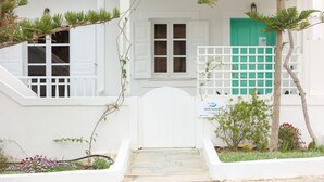 A white building with a green door, white shutters, and a small garden with flowers and plants. - Azul Home - Ahilli Slow Living (Καμάρι)