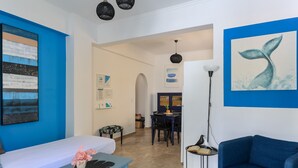 A modern living room with a blue sofa, a white bed, and a dining area with a table and chairs. - Azul Home - Ahilli Slow Living (Καμάρι)