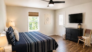 Un dormitorio con una cama, ventilador de techo, televisor, cómoda y una silla.