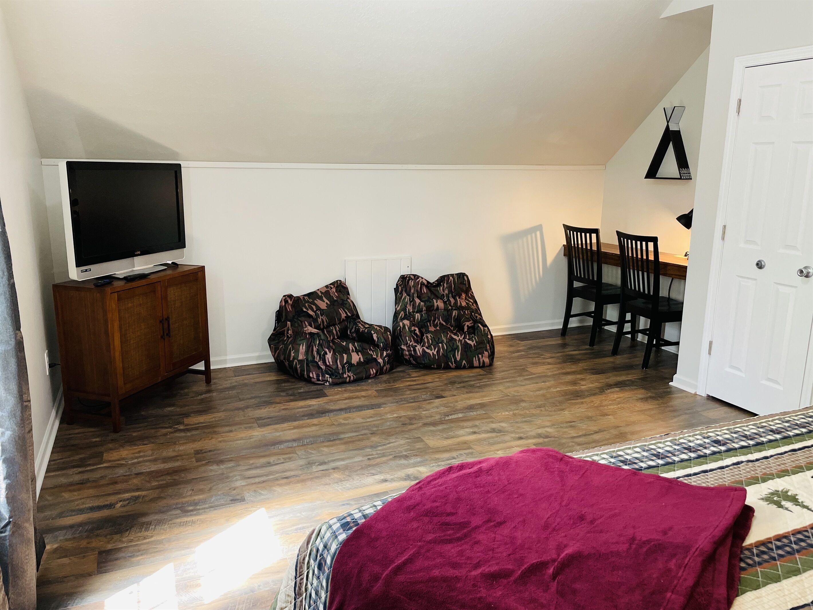 A room with a television on a wooden cabinet, two camouflage bean bags, a dining table with chairs, and a patterned rug.