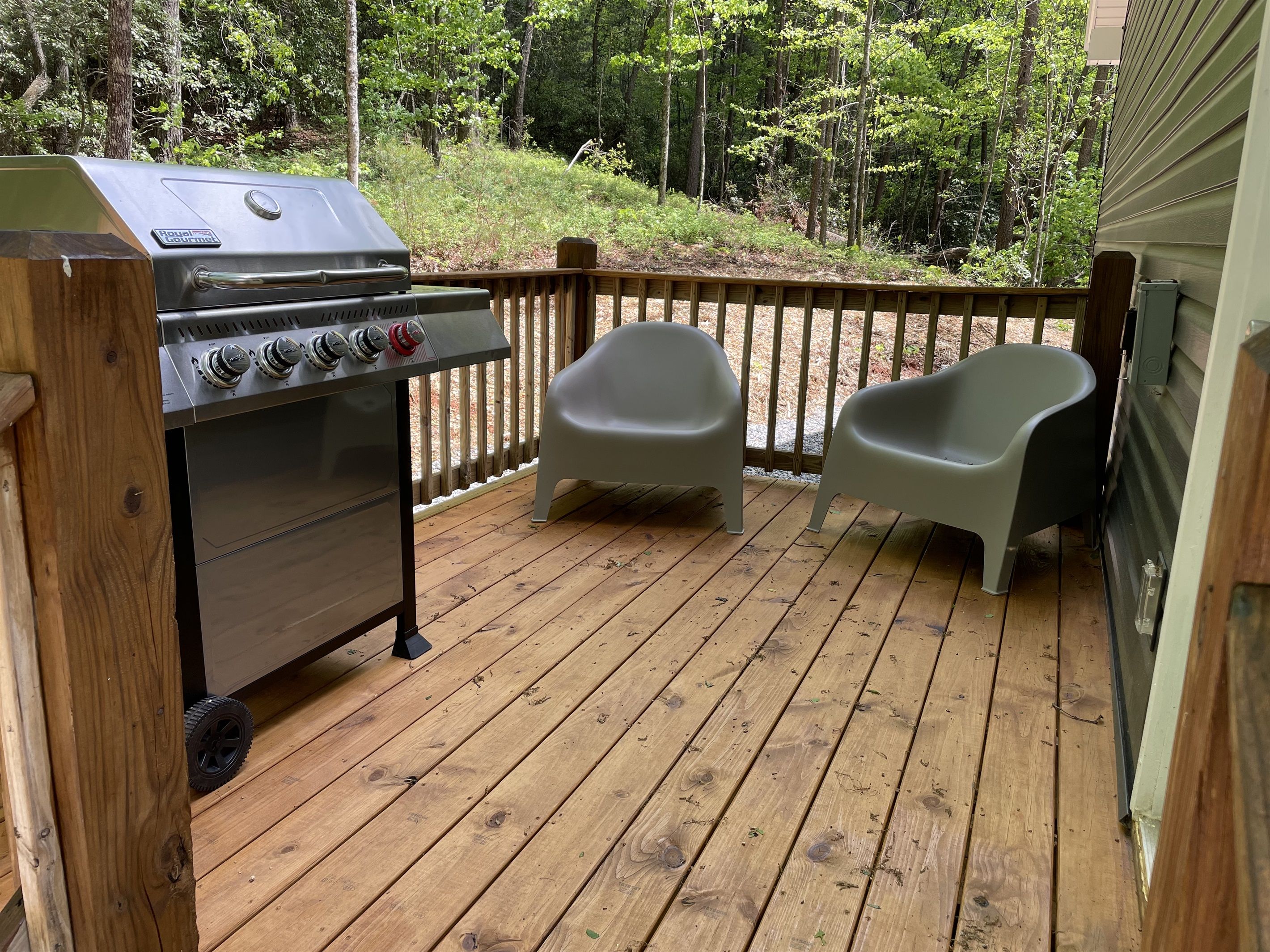 A wooden deck with a grill and two plastic chairs.