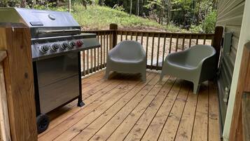 A wooden deck with a grill and two plastic chairs.