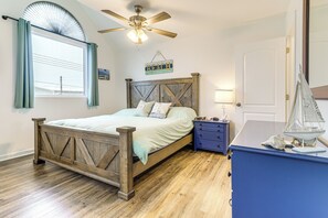A bedroom with a wooden bed, a ceiling fan, a window with curtains, a nightstand, a dresser, and a sailboat decoration. - Topsail Beach Vacation Rental: Idyllic Ocean Views (Topsail Beach)