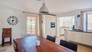 A dining area with a wooden table, chairs, a clock, and a kitchen in the background. - Beautiful home in Fayence (Fayence)