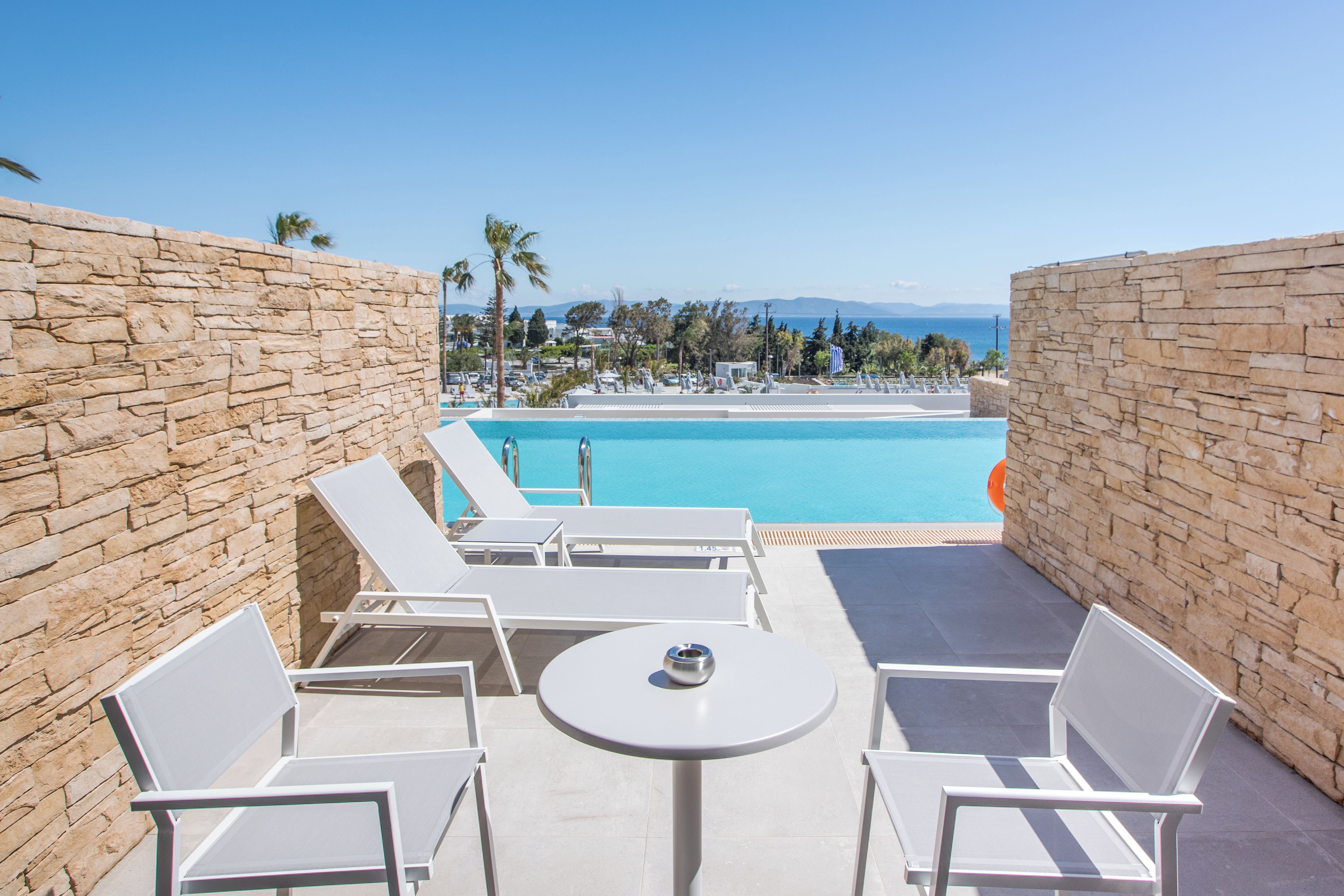A poolside area with stone walls, white lounge chairs, and a table.