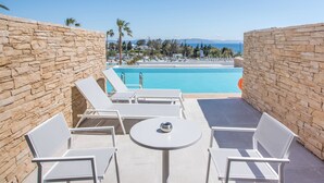 Un espace aménagé au bord de la piscine, avec des murs en pierre, des chaises longues blanches et une table.