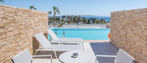 A poolside area with stone walls, white lounge chairs, and a table.