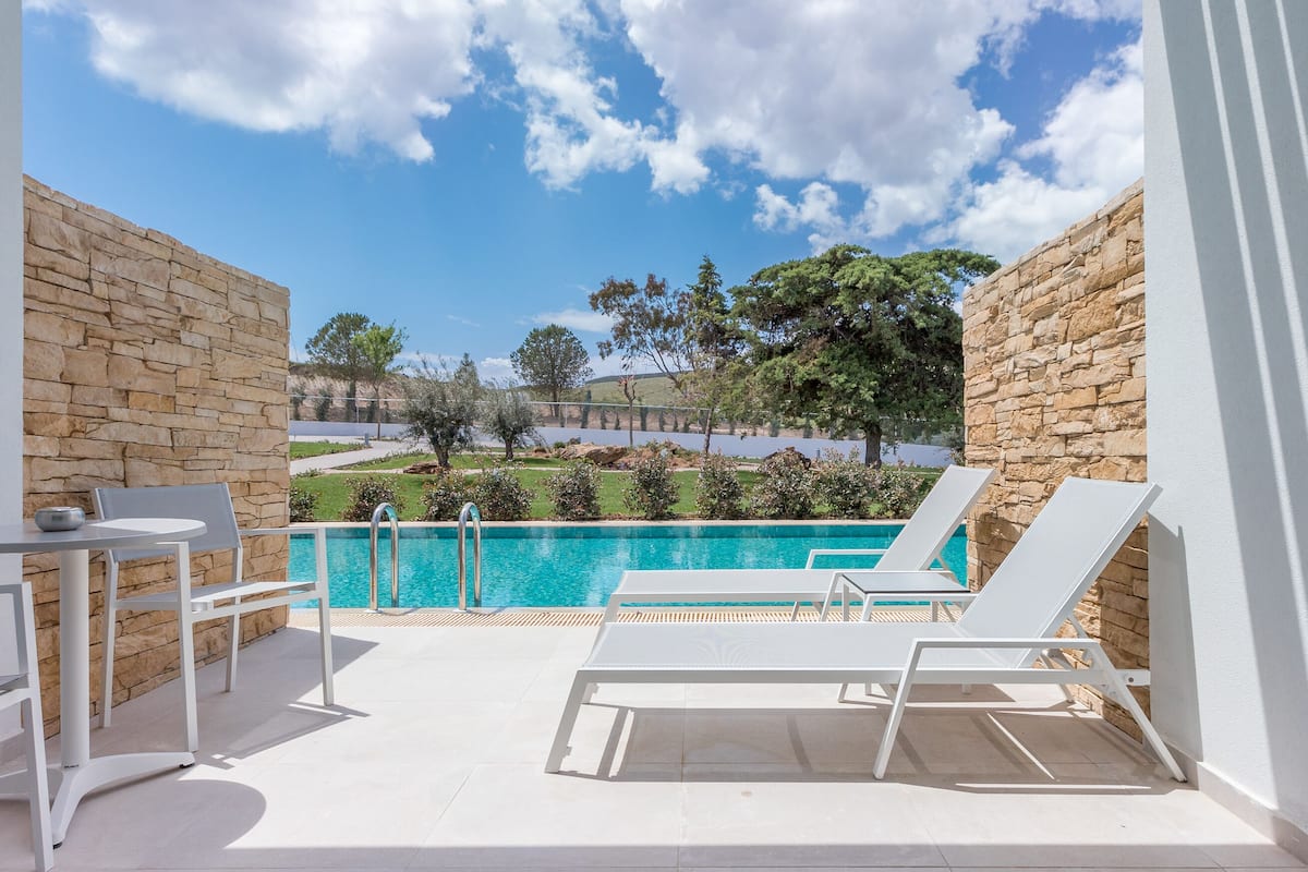 A balcony with a pool, white furniture, and stone walls.