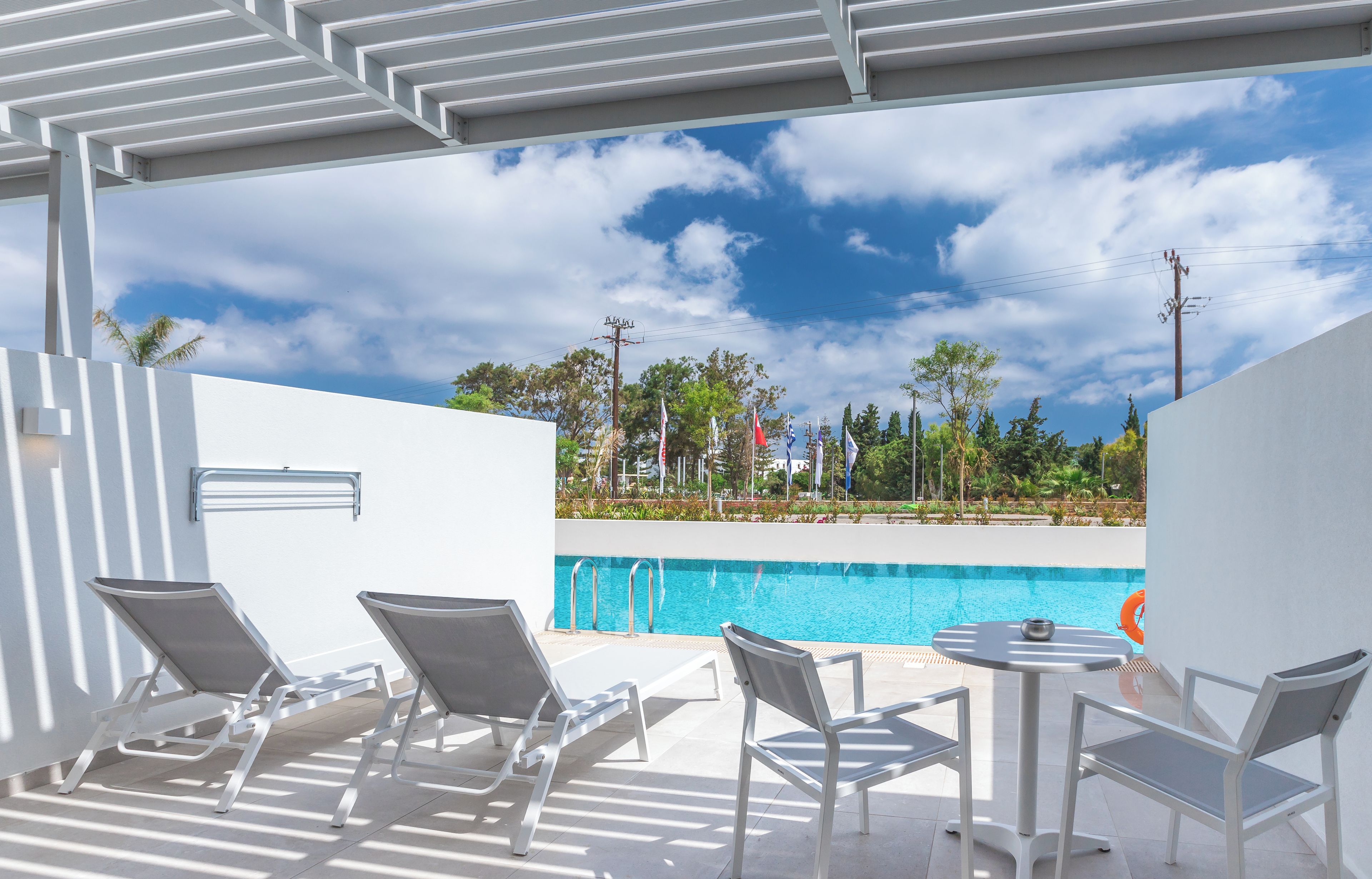 Zona de piscina con sillones de descanso y una mesa, con vista a una alberca y un jardín ajardinado.