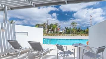 Zona de piscina con sillones de descanso y una mesa, con vista a una alberca y un jardín ajardinado.
