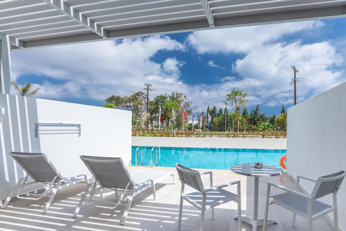 A poolside area with lounge chairs and a table, overlooking a swimming pool and a landscaped garden.