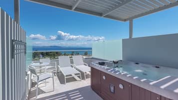 Una terraza en la azotea con jacuzzi, sillones de descanso y balaustrada de vidrio con vistas panorámicas.