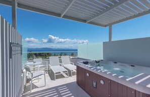A rooftop terrace with a hot tub, lounge chairs, and a glass balustrade overlooking a scenic view. - Blue Lagoon Ocean (Kos)