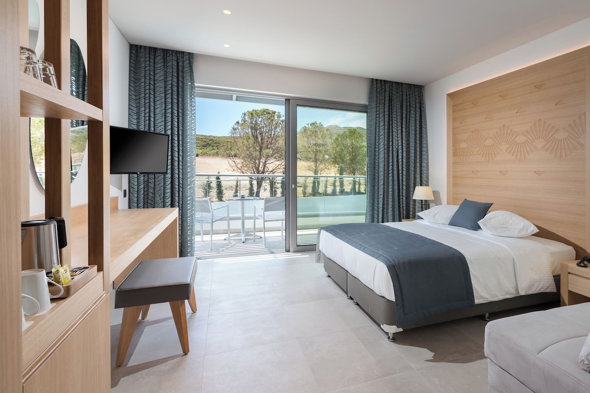 Habitación de hotel moderna con una cama grande, un escritorio, una silla y un balcón con vistas al exterior.