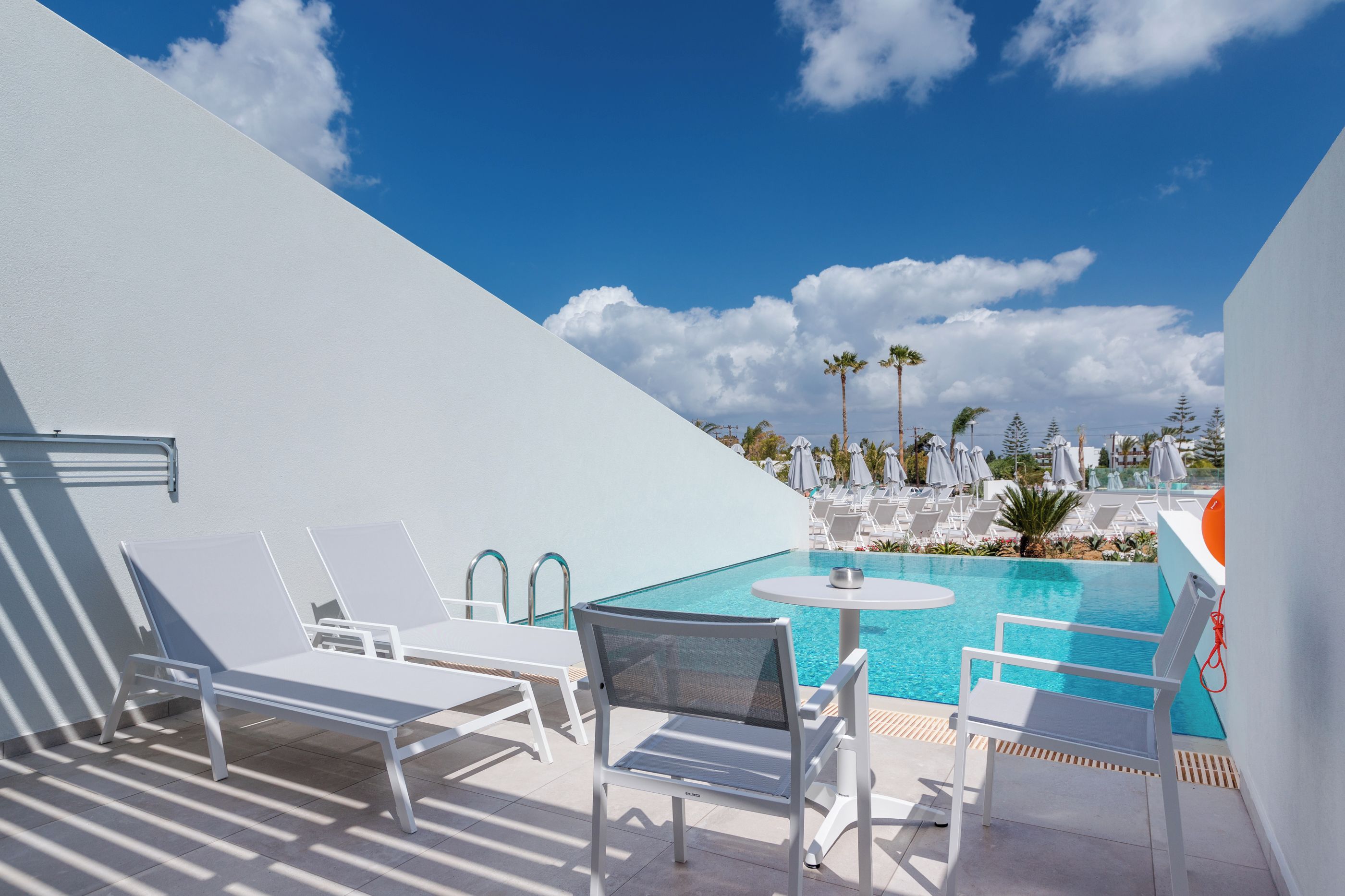 Zona de piscina al terrat amb gandules blanques i una taula petita, tot envoltat d'una paret blanca i un cel blau clar.