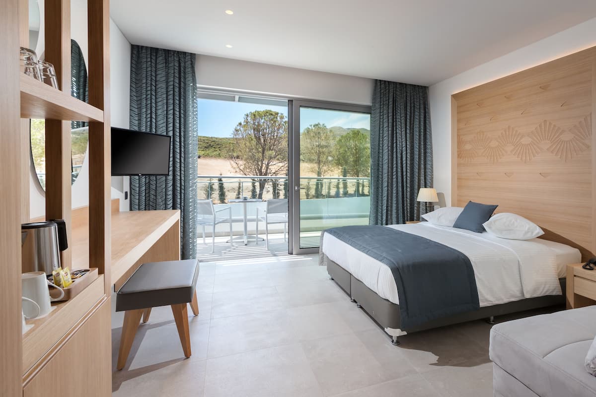 Habitación de hotel moderna con una cama grande, un escritorio, una silla y un balcón con vistas al exterior.