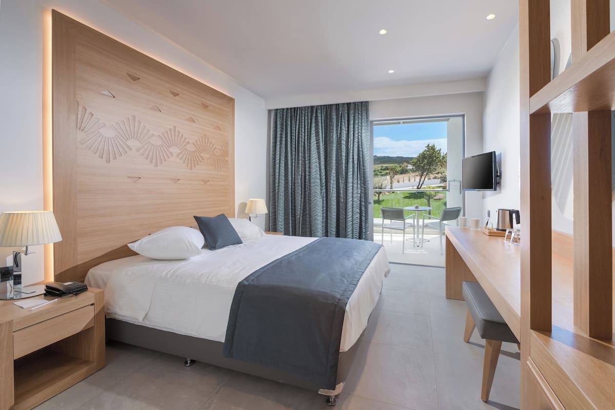 A modern hotel room with a bed, bedside table, lamp, and a view of the outdoors.