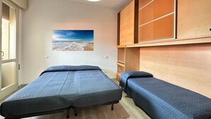 Een kamer met twee bedden, een groot raam en een schilderij van een strandgezicht.