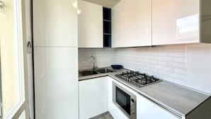 Een kleine keuken met witte kastjes, een gasfornuis, een spoelbak en een blauwe kom.