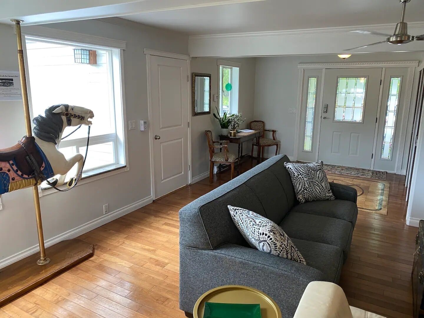 A living room with a grey sofa, a wooden floor, and a carousel horse by the window.