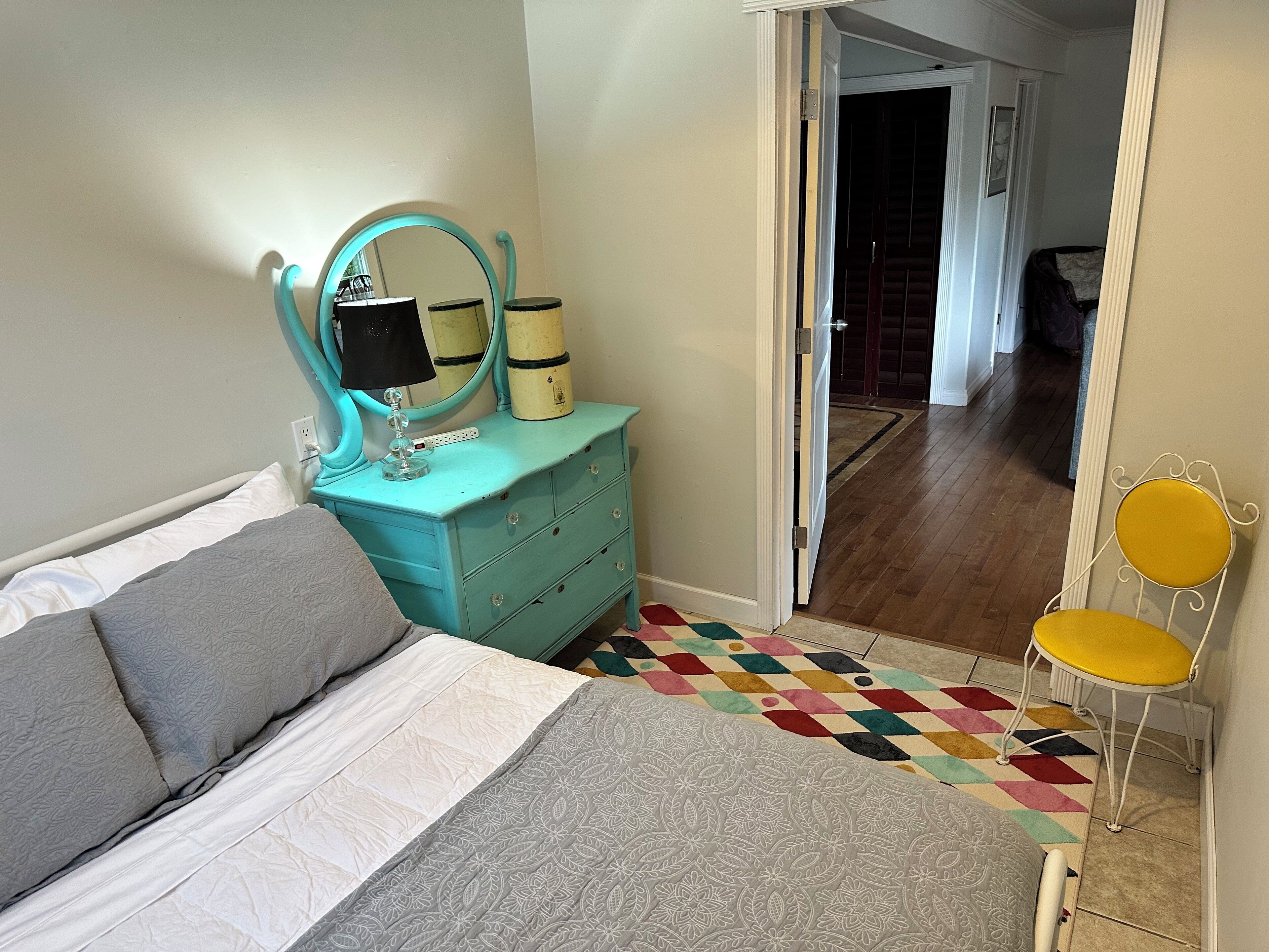A bedroom with a bed, a dresser with a mirror, a lamp, and a chair.