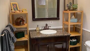 A bathroom with a dark wood vanity, a white sink, a large mirror, and a toilet. There are shelves with various items and a towel rack.