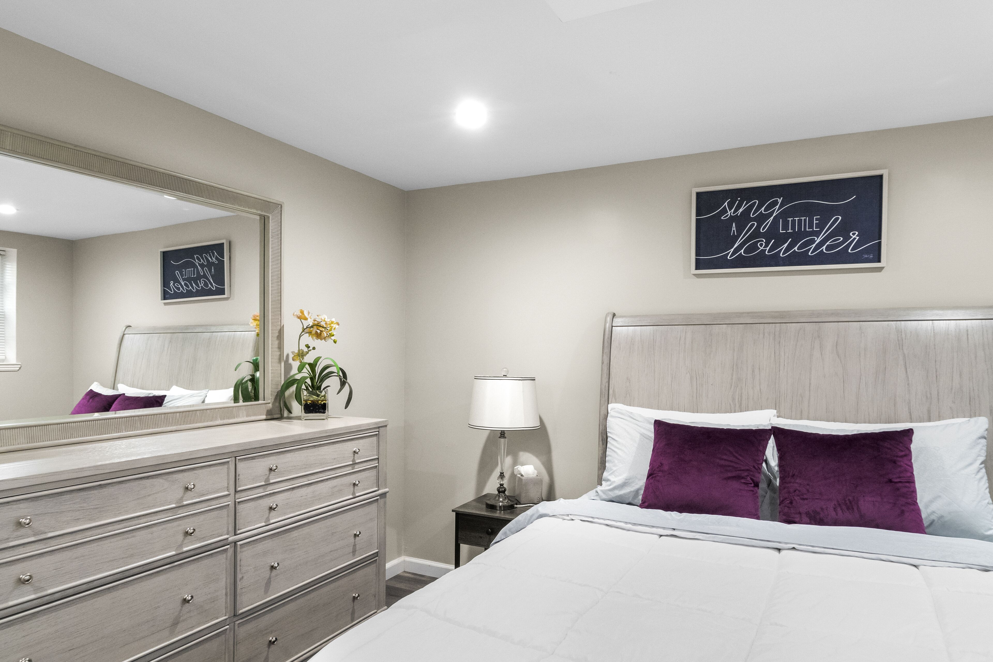 A bedroom with a bed, dresser, nightstand, lamp, and wall decor.