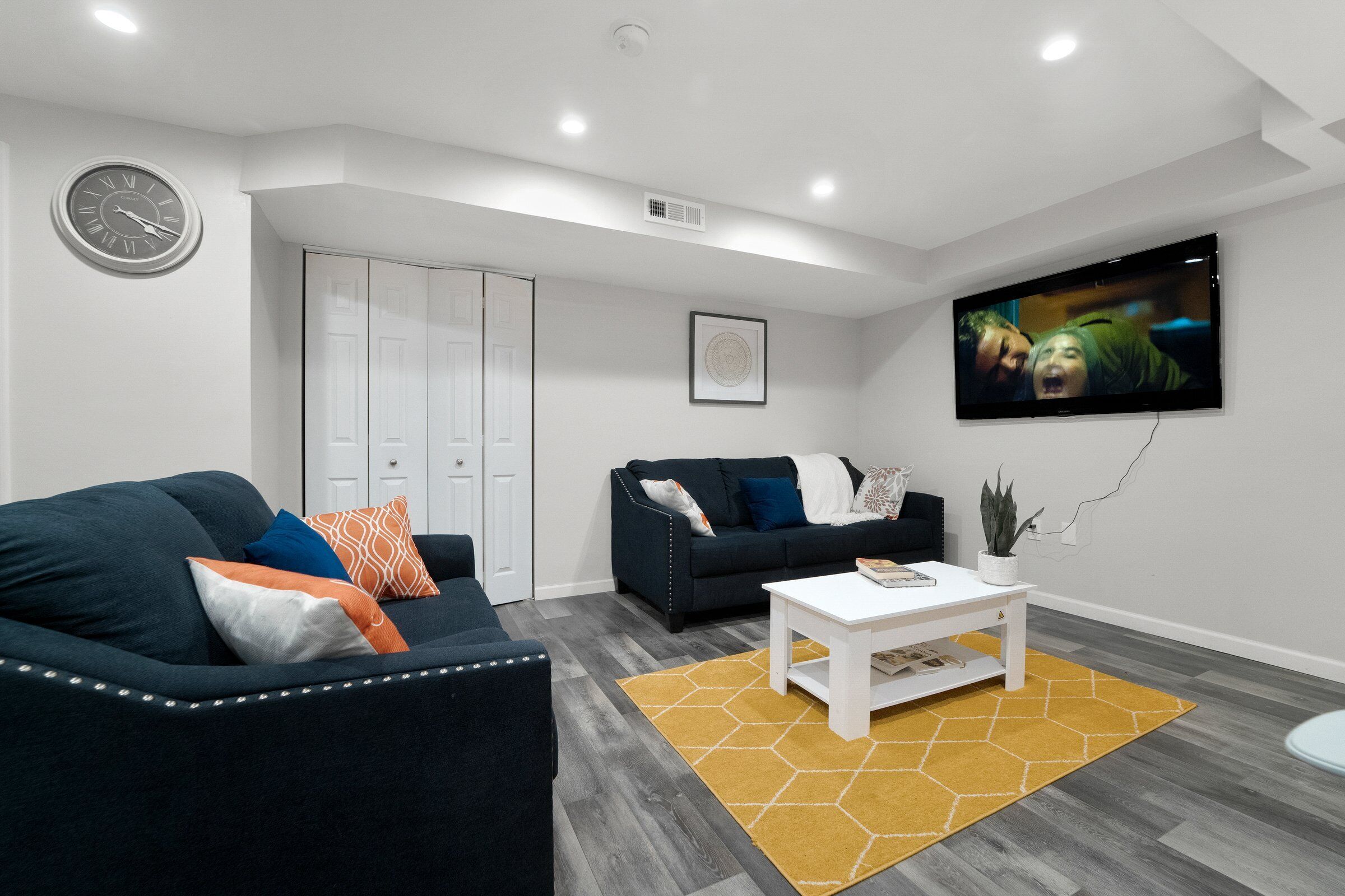 A modern living room with two dark sofas, a white coffee table, and a yellow rug.