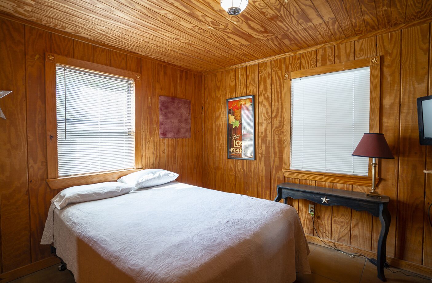 A wooden-paneled room with a bed, a nightstand, a lamp, and a television.