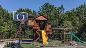 Une structure de jeu en bois comprenant un panier de basket, un toboggan et une balançoire.