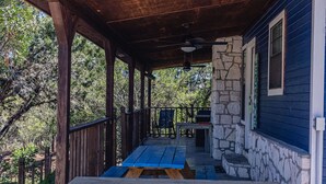 Un espace extérieur abrité, doté d’une table et de bancs en bois, de murs en pierre et offrant une vue sur les arbres.