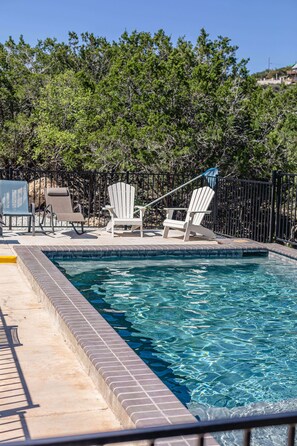 A swimming pool with a tiled edge, surrounded by a fence and trees.