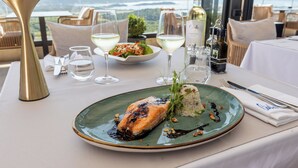 A dining table with a plate of salmon, white wine glasses, and a bottle of wine. - Royal Blue Resort & Residence (Kotor)