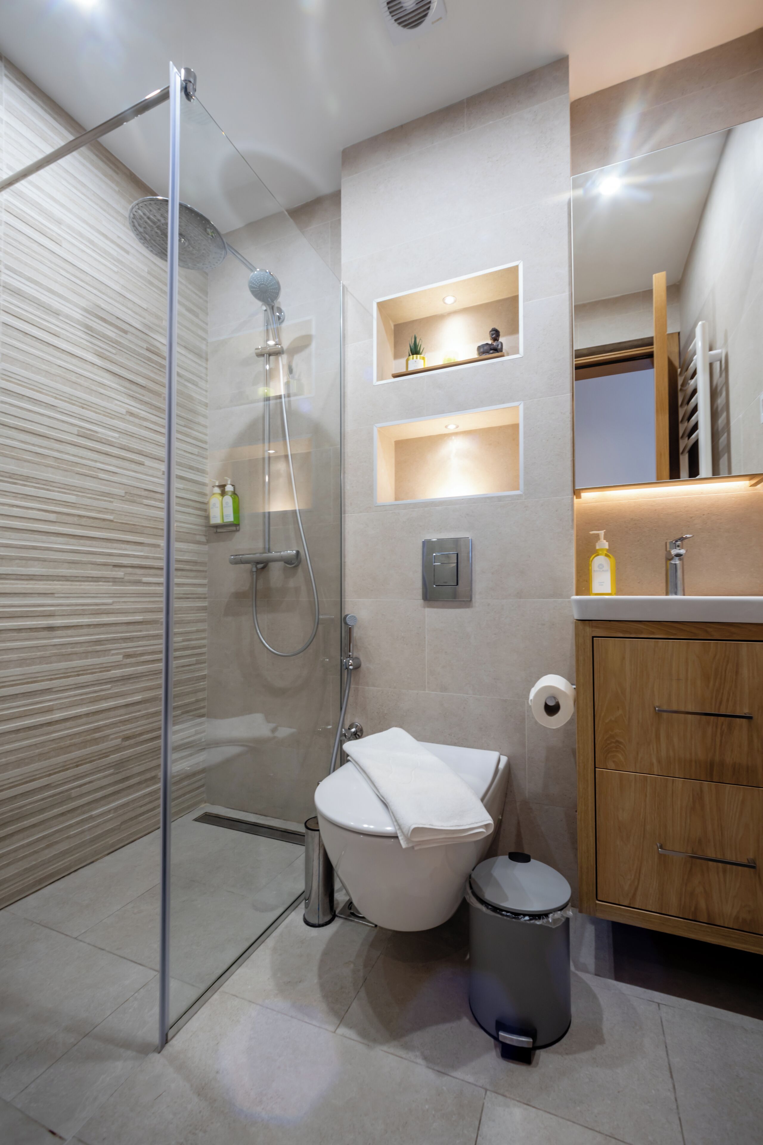 A modern bathroom with a glass-enclosed shower, a toilet, a trash bin, and wooden cabinets.