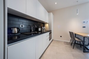 Una cocina moderna con armarios blancos, encimeras negras y electrodomésticos de acero inoxidable. Cuenta con un comedor con mesa y sillas.